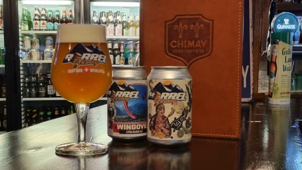 I migliori bar di Interlaken 2 Bicchieri e lattine di birra della Rappi Brewing su un bancone, circondati da vari tipi di birra sullo sfondo.