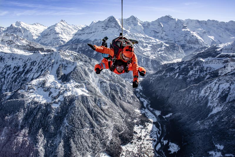 Actividades de invierno Interlaken Parte 3 2 una persona con un traje naranja desde una cuerda sobre una montaña nevada