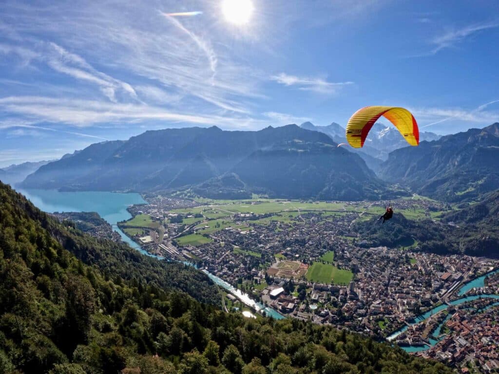 Parapendio o paracadutismo: quale volo è più adatto a te? 3 Un volo in parapendio su Interlaken, in Svizzera, con vista su laghi e montagne sotto un cielo azzurro e un sole splendente.
