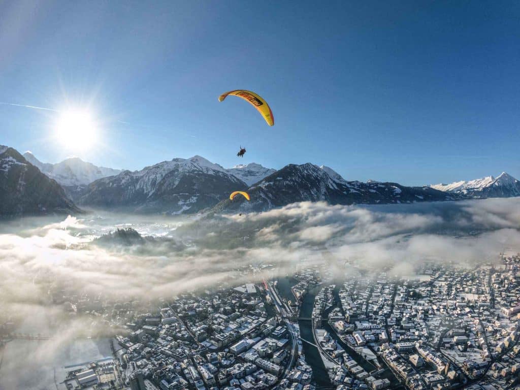 Vuela en parapente sobre los Alpes nevados, con impresionantes paisajes invernales y cielos despejados a la luz del sol.