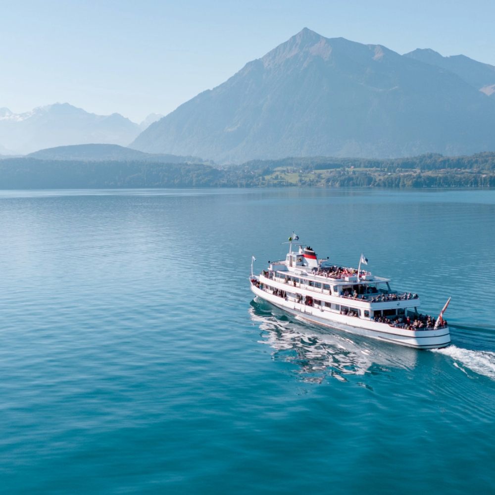 Bateau de croisière naviguant sur un lac alpin avec montagnes en arrière-plan par temps clair et ensoleillé.