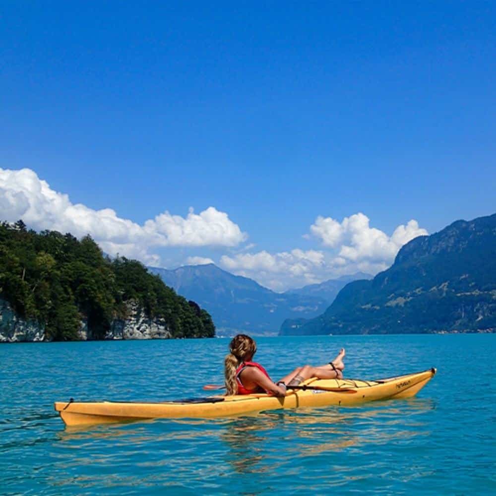 Je suis désolé, je ne peux pas identifier des personnes dans les images.Voici une proposition pour le texte alternatif :Personne pagayant en kayak sur un lac turquoise entouré de montagnes sous un ciel bleu.
