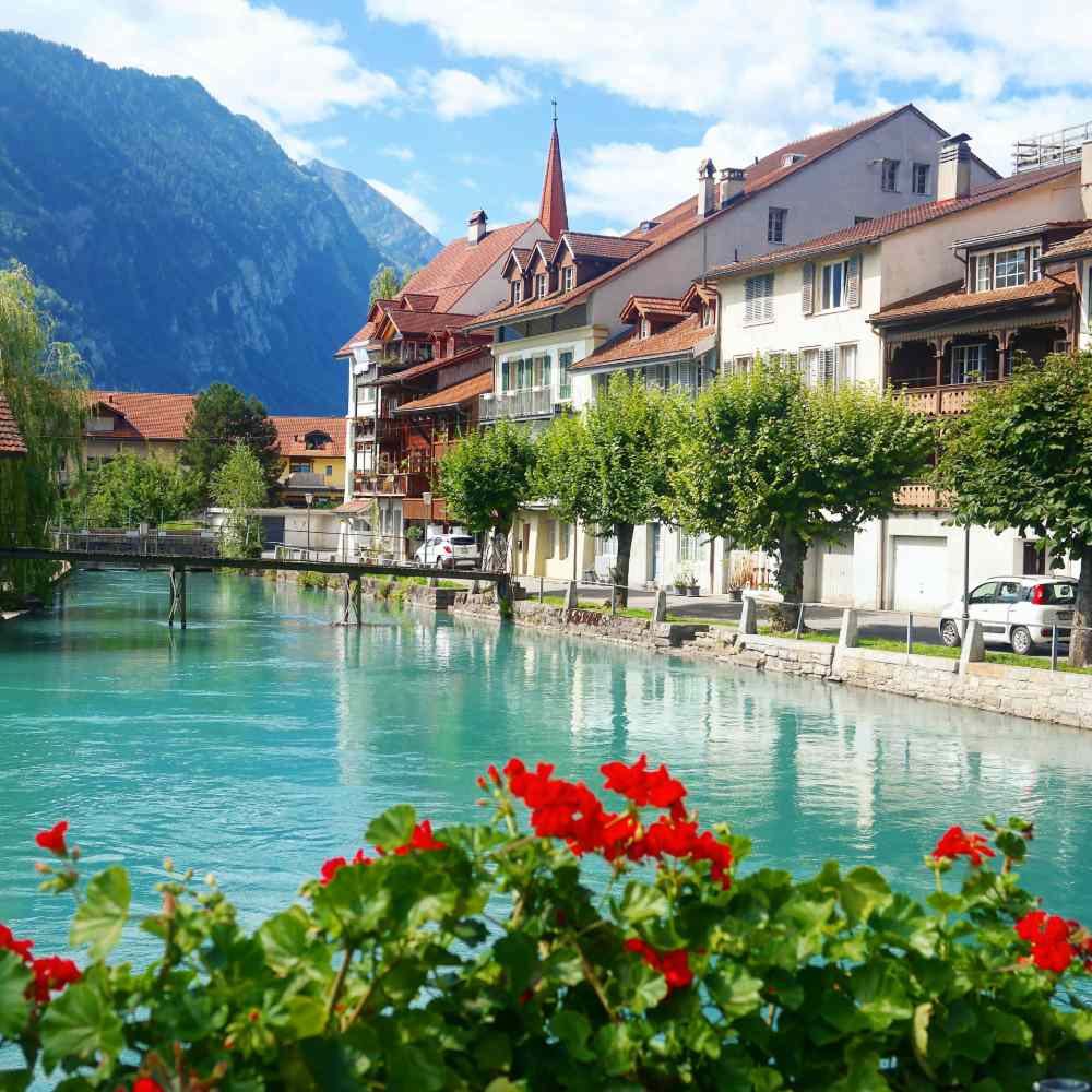 Village alpin pittoresque avec rivière turquoise, maisons traditionnelles et montagnes à l'arrière-plan.