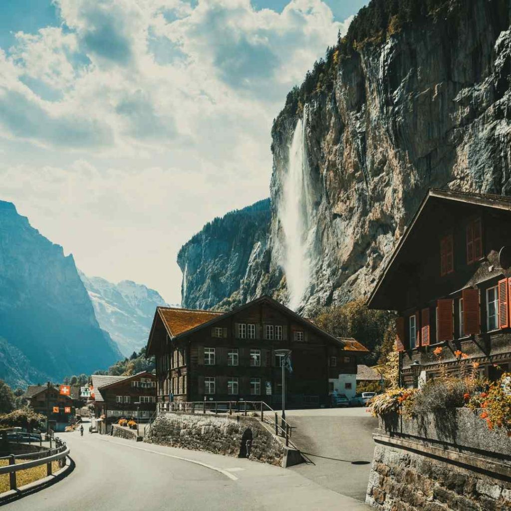 Village suisse pittoresque avec cascade impressionnante et chalets traditionnels en bois. Paysage alpin typique.