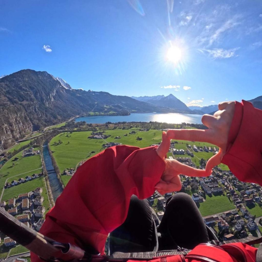 Parapente au-dessus des montagnes et d'un lac scintillant sous le soleil, avec vue sur une vallée verdoyante.