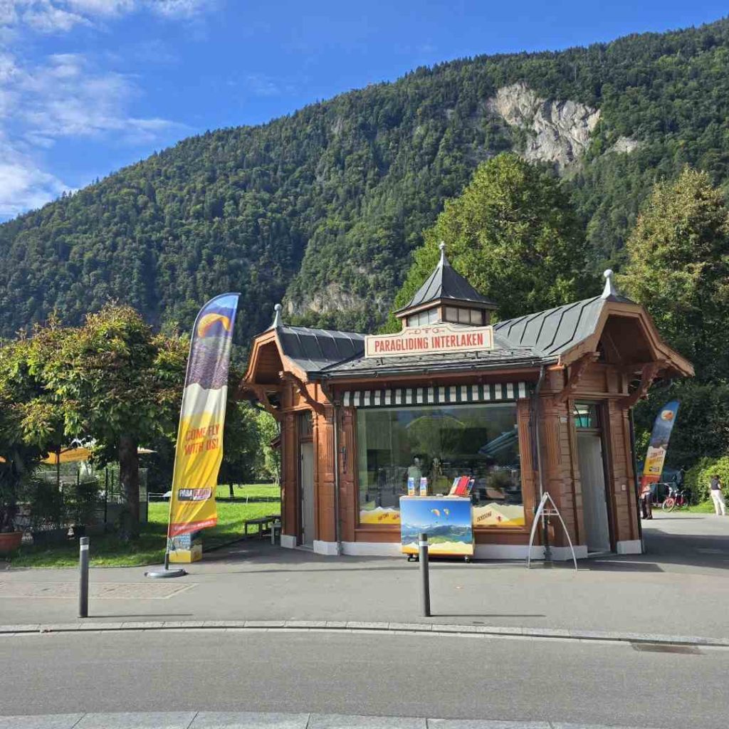 Boutique de parapente à Interlaken avec montagne verdoyante en arrière-plan, ciel bleu et ambiance estivale.
