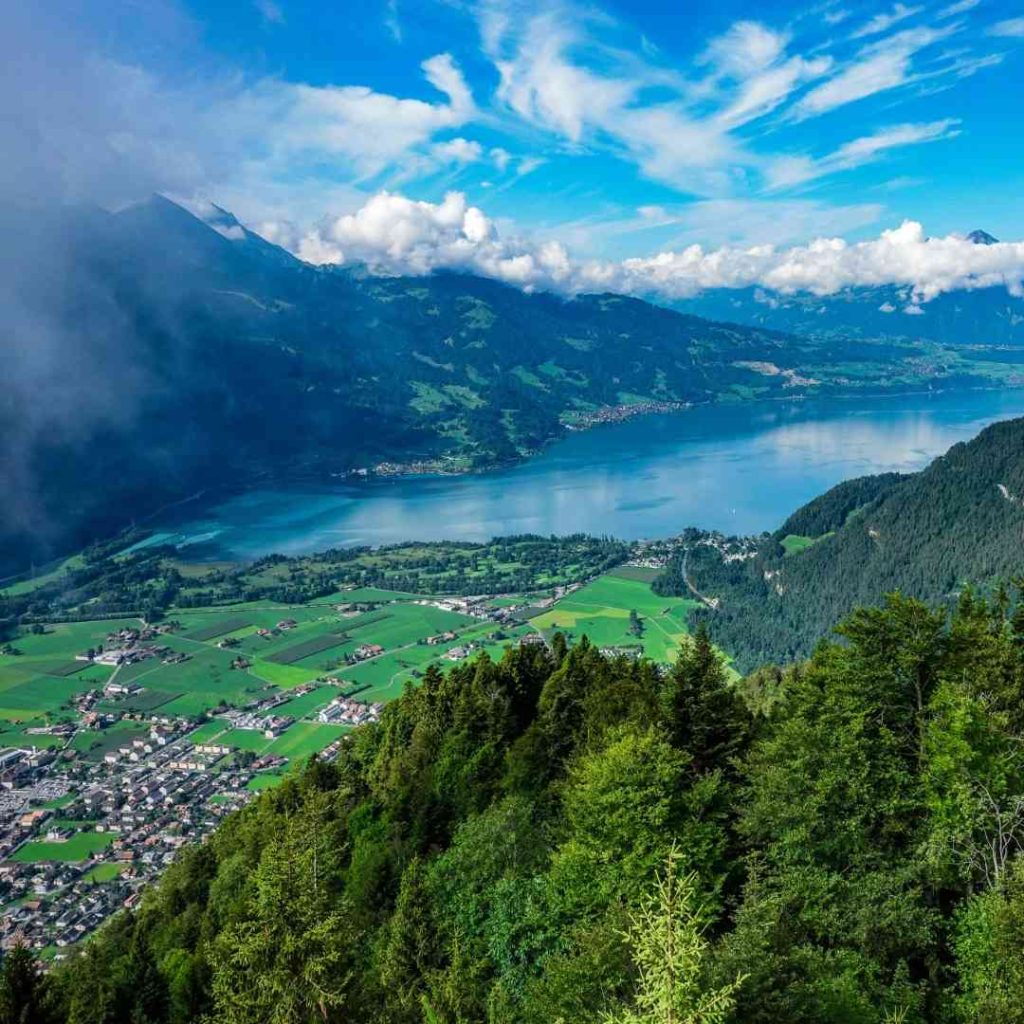 Panorama alpin avec lac et vallée verdoyante sous un ciel bleu parsemé de nuages. Paysage naturel enchanteur.