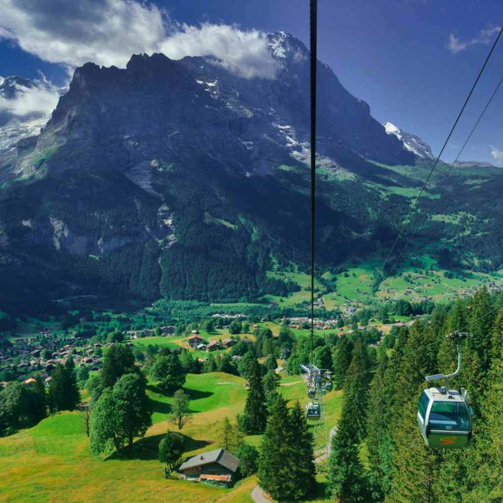 Téléphérique survolant des montagnes verdoyantes par temps ensoleillé, offrant une vue panoramique saisissante.