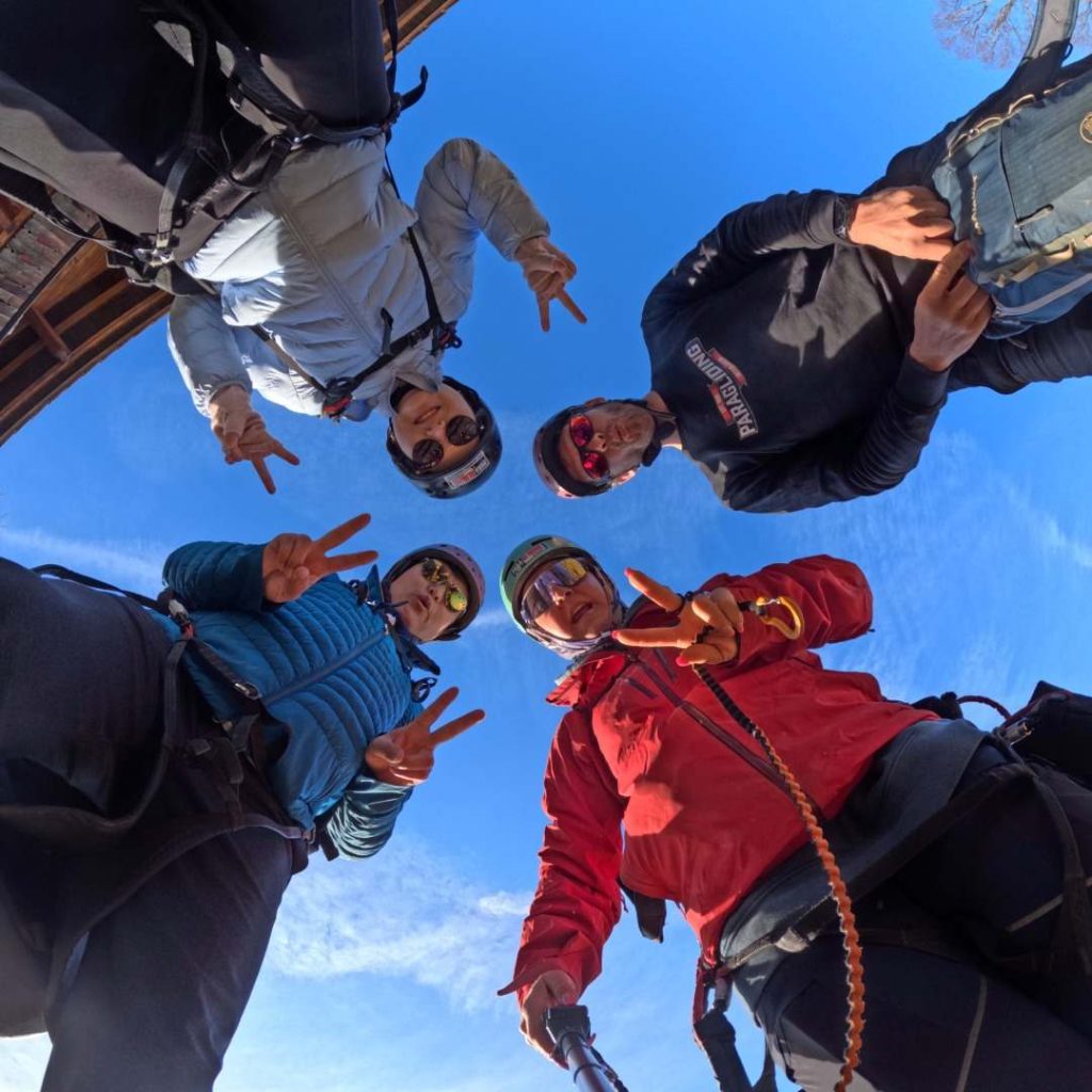 Quatre personnes en tenue d'escalade font un signe de paix sous un ciel bleu.